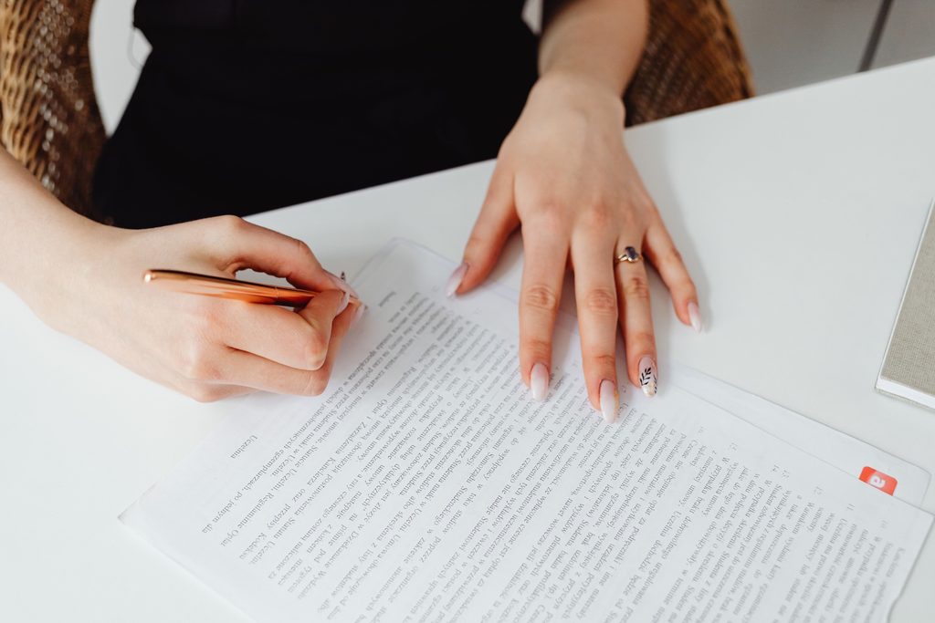 Mains d'une femme annotant un document au stylo sur un bureau blanc