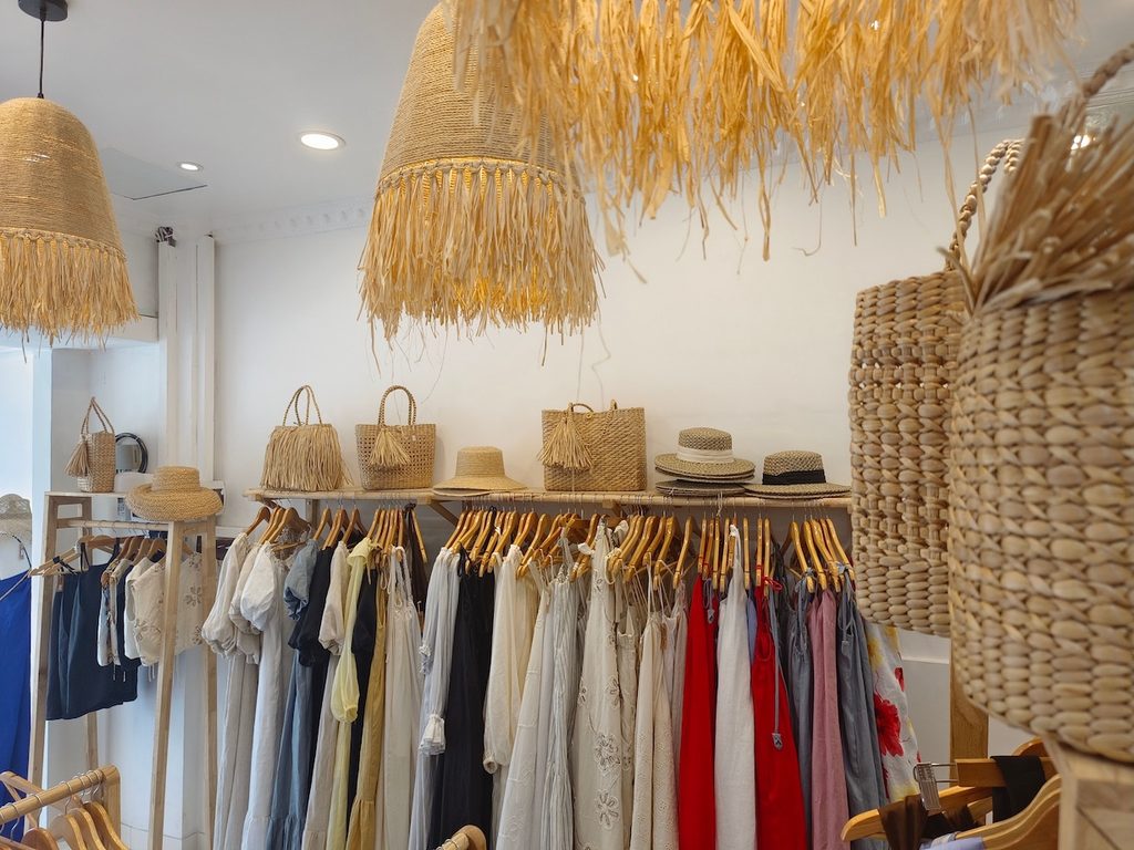 Portants de robes et sacs en paille dans une boutique de prêt-à-porter