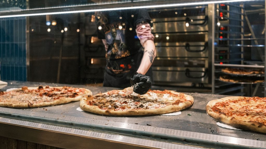 Pizzaiolo garnissant des pizzas derrière la vitre d'un comptoir